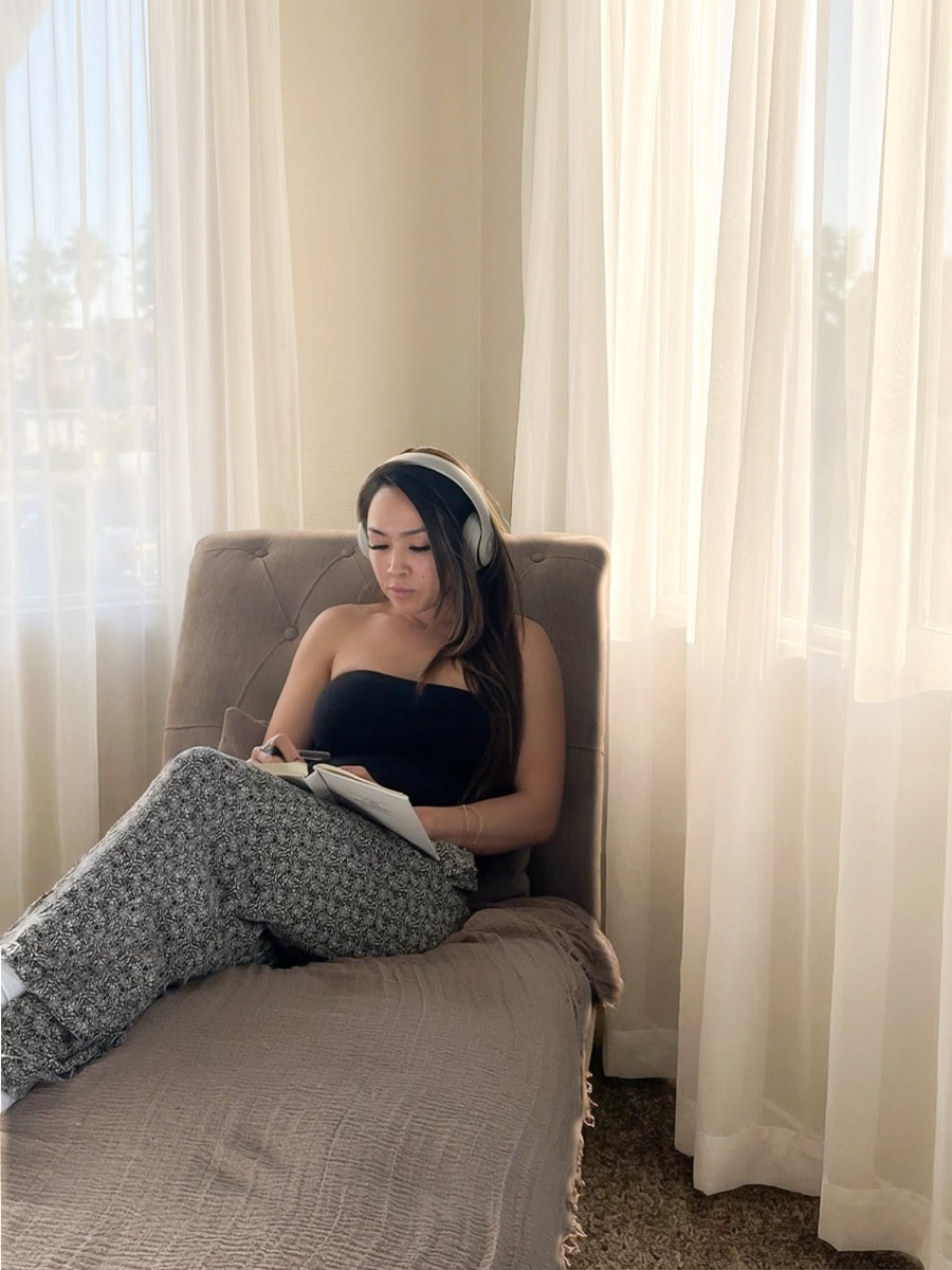 Woman journaling on a chaise lounge with headphones in a sunlit room — mindful business planning and self-care for beauty entrepreneurs.